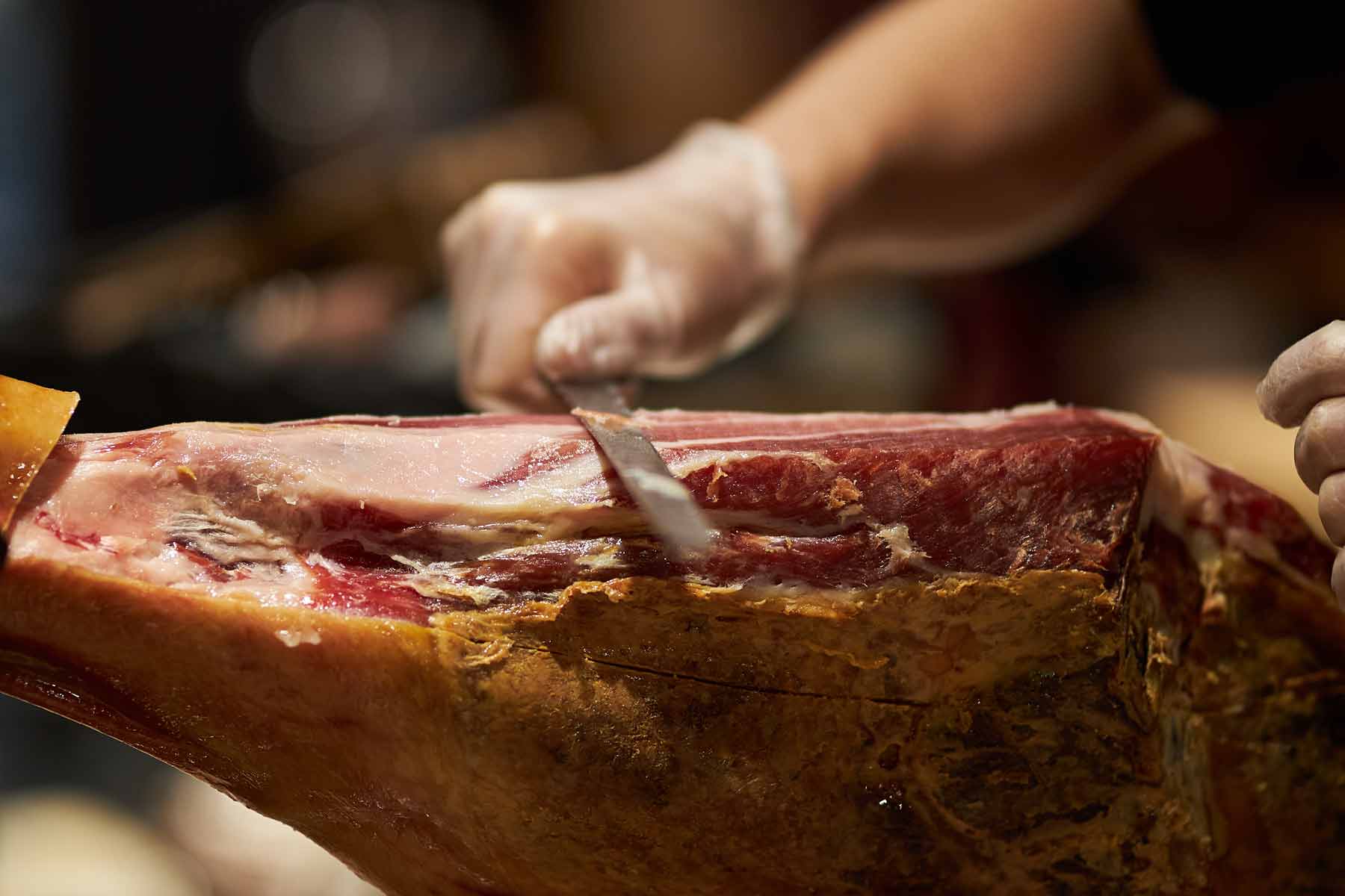Persona adulta cortando un jamón ibérico a cuchillo